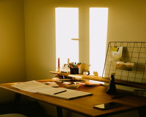 A clean domestic workspace setup with a notebook wooden desk and natural light coming from a window